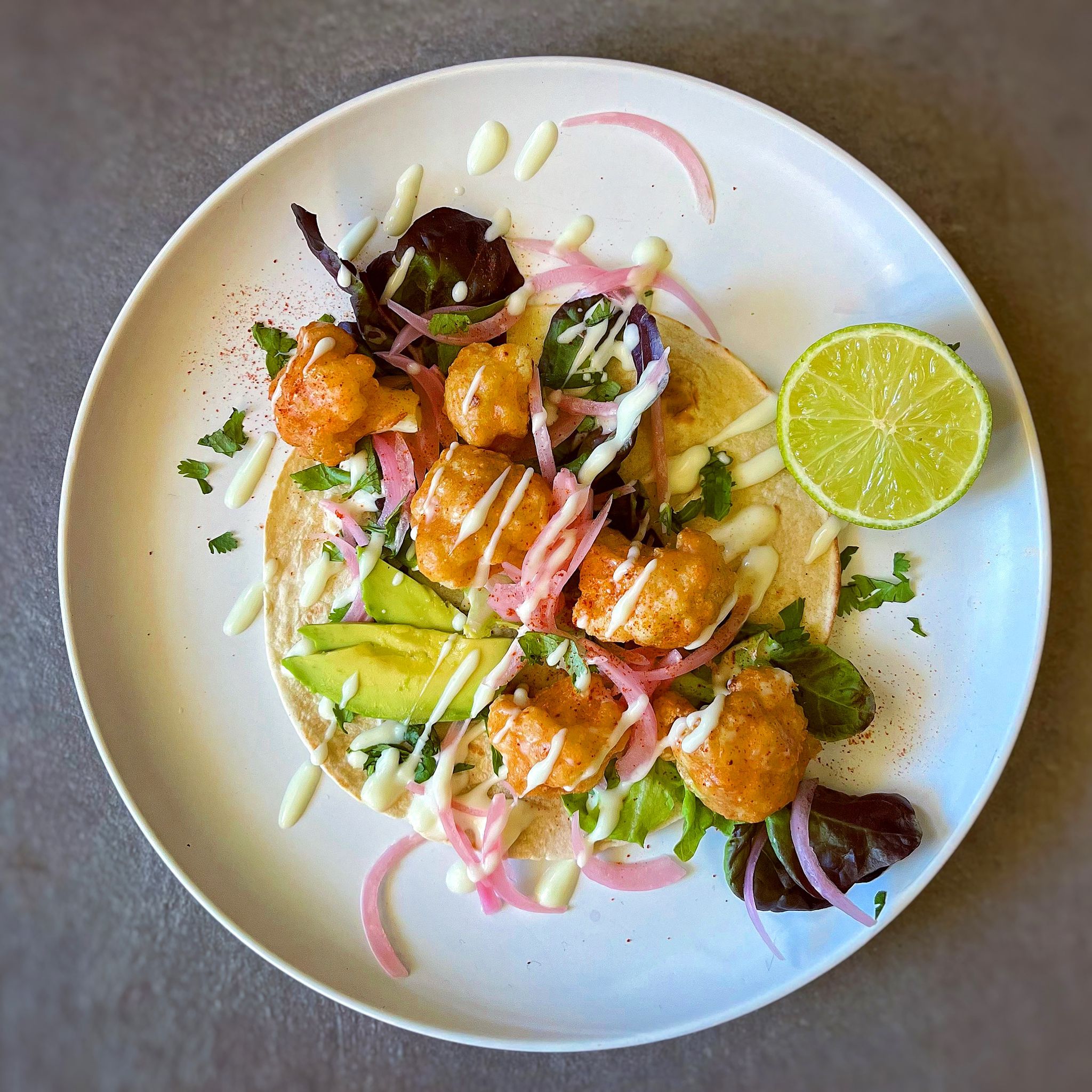 Crispy Baja cauliflower tacos with pickled red onions, greens, and vegan lime mayo