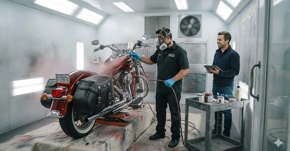 A red cruiser motorcycle being professionally painted in a spray booth by a technician in safety gear, while another person observes with a tablet.