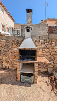 Barbacoa de ladrillos con chimenea con pared de adobe detrás, vista en el jardín de la Posada