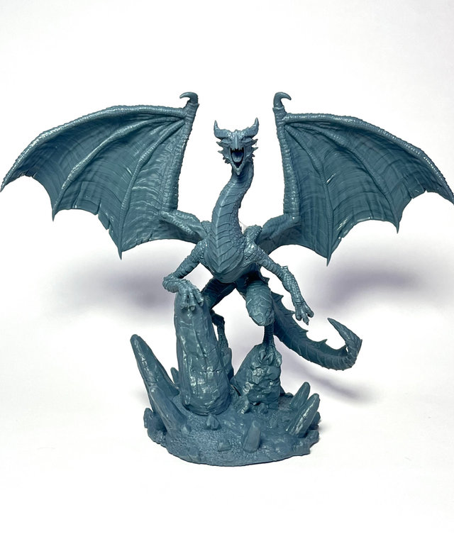Miniatura de RPG de dragão com asas abertas sobre base de rochas