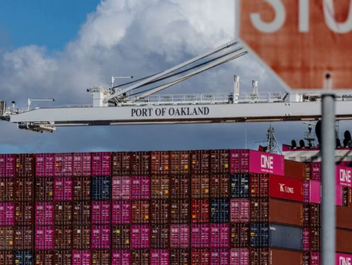 Many shipping containers on a cargo ship in the Port of Oakland. The name of the location can be seen on a small platform above the containers. At the front of the picture, there is a red stop sign.