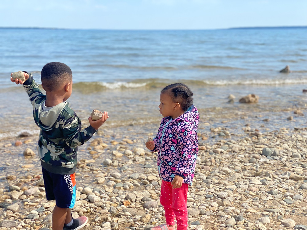 Two young Black children playing by the shore of the lake with rocks and small waves