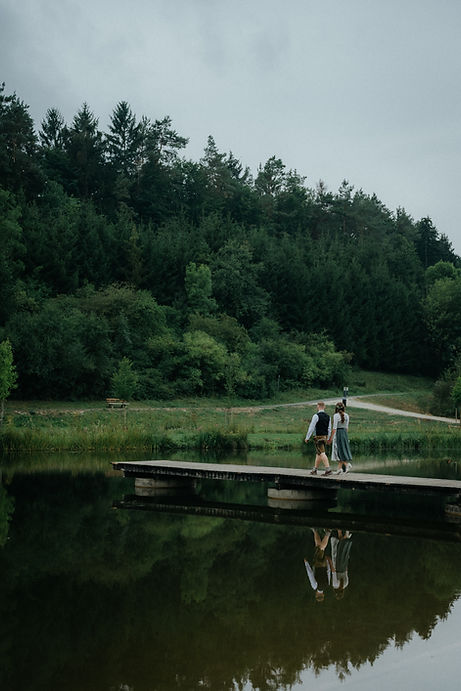 Ein Hochzeitspaar läuft über einen Steg an einem See und schaut in die Ferne