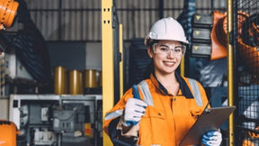 Woman on industrial job site smiles and gives a thumbs up