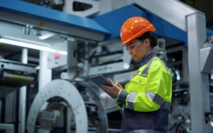 Woman wearing PPE in an industrial worksite reviews tablet