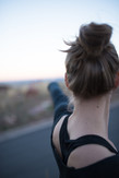 Close up of a girl performing yoga, picture taken from behind showing her hair in a bun with left arm pointing toward the distance. Hinting a warrior pose.