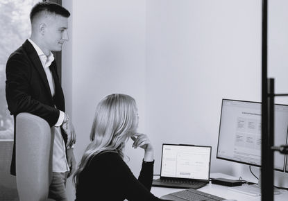 Zwei Personen analysieren gemeinsam Daten auf einem Computerbildschirm und Laptop im Büro, um die kosten Fenstertausch und mögliche Fördermittel zu prüfen.