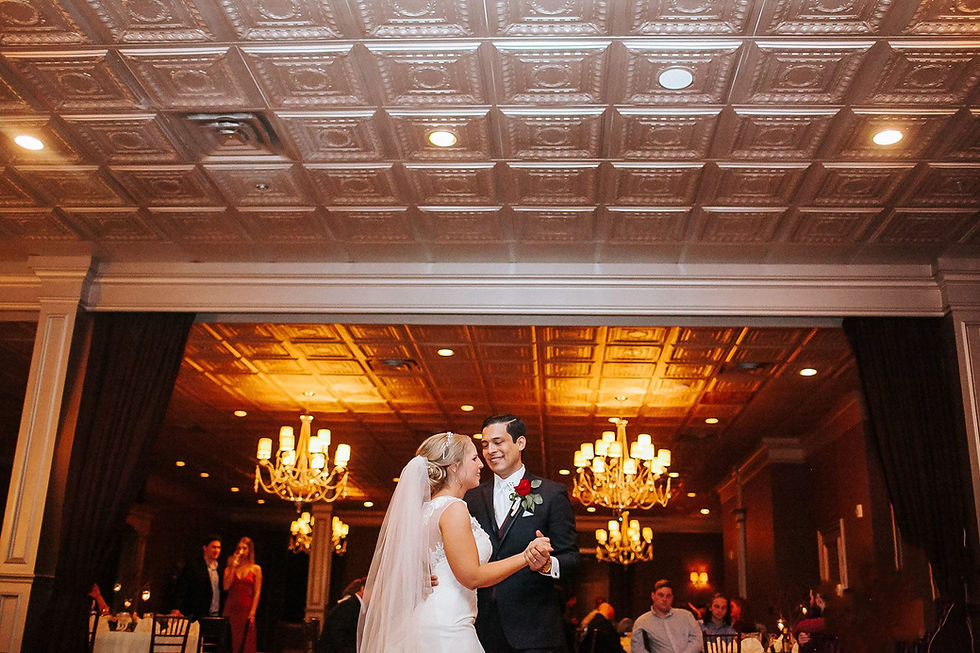 A couple sharing a dance in the candlelit Royal Affairs Ballroom, framed by crystal chandeliers and an antique pressed-tin ceiling.