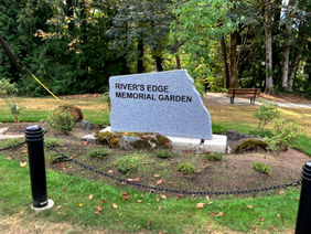 "RIVER'S EDGE MEMORIAL GARDEN" stone sign in a tranquil park.