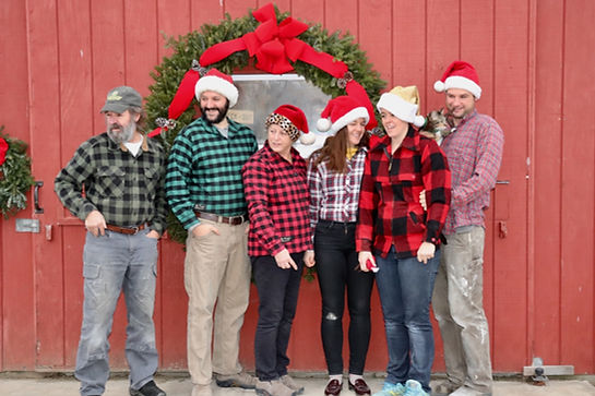Six people stand in front of a red barn with a wreath.