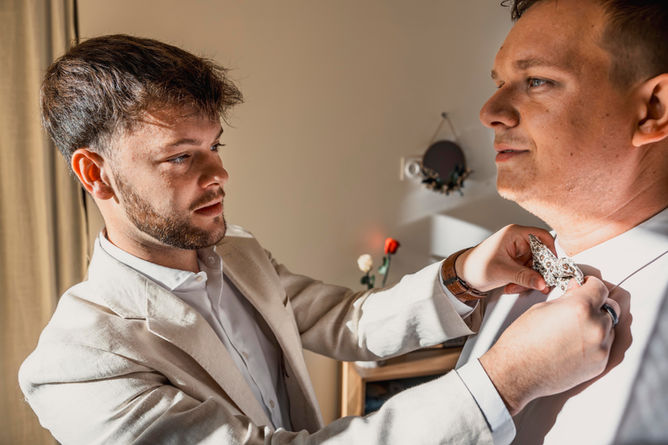 Un témoin du marié ajustant le nœud papillon du marié en intérieur.