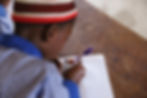 Child writing in an exercise book at a wooden desk in class