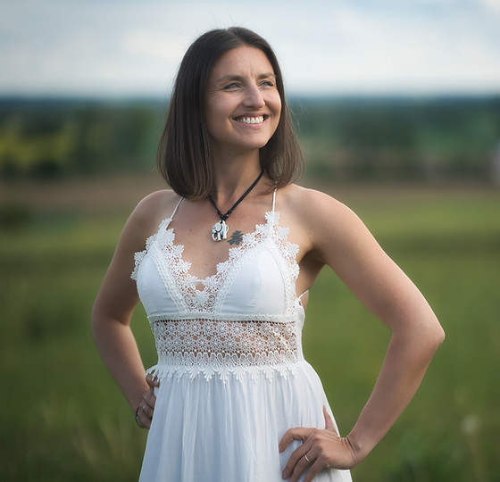 Eine Frau im weißen Kleid steht auf einer grünen Wiese und sieht lächelnd zur Seite