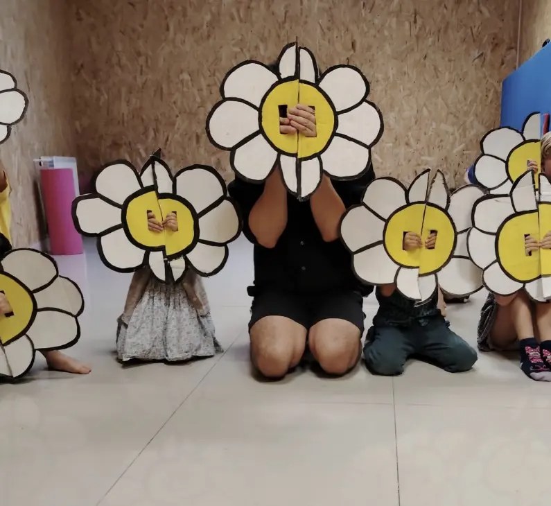 Enfants cachés derrière de grandes fleurs en carton lors de l'activité de fin d'année