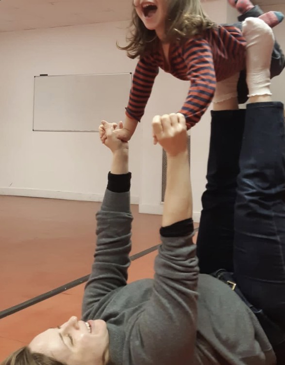 Une mère allongée soulève sa fille à bout de bras pendant un atelier parent-enfant