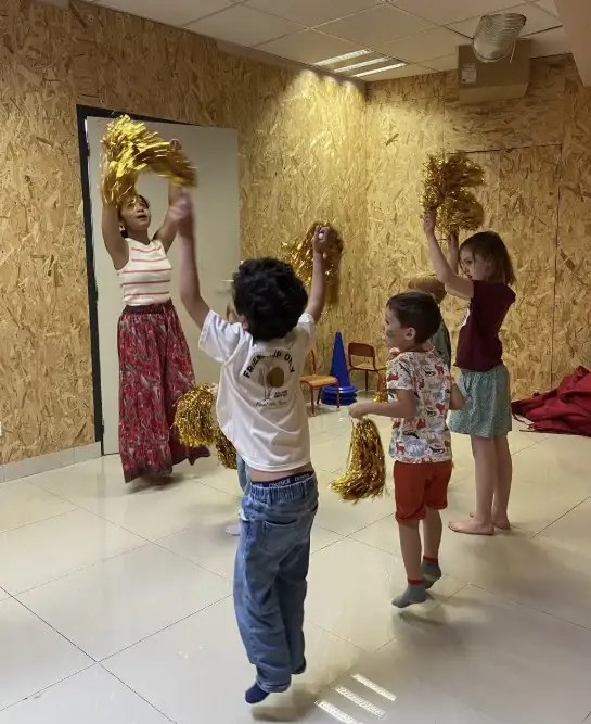 Enfants et intervenante dansent avec des pompons dorés
