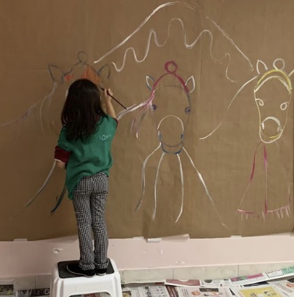 Une enfant peint une grande fresque de chevaux sur du papier kraft