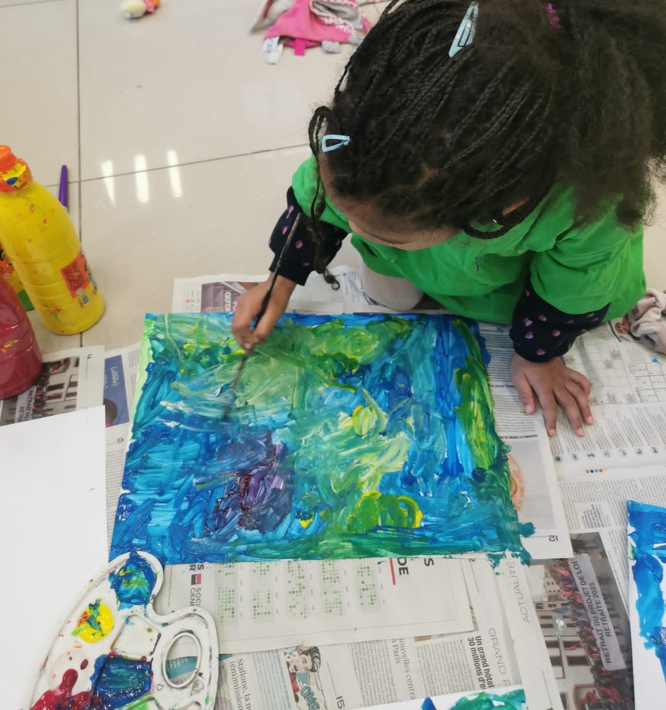 Une enfant peint une grande toile bleue, vue de dessus