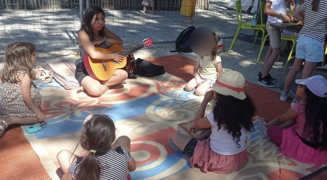 Atelier musique en plein air avec une intervenante à la guitare pendant un stage de vacances