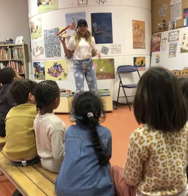 Un groupe d'enfants assis, de dos, écoute une intervenante debout devant des affiches