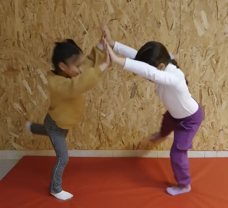 Deux enfants font un exercice de yoga en miroir sur un tapis orange
