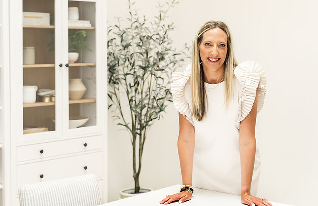 Kalissa standing and leaning on desk smiling in dress giving an approachable feeling for people to reach out for a discovery call..
