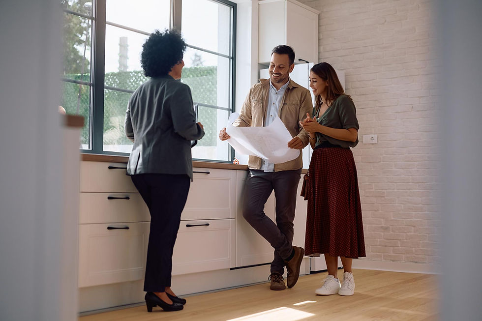 Three people reviewing a floor plan in a bright kitchen with white cabinets and large windows.