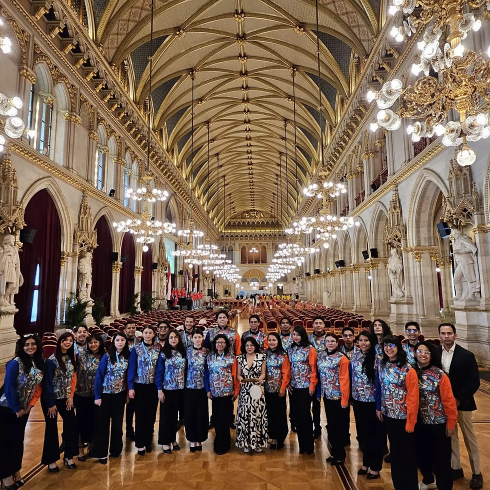Grupo posando en un gran salón histórico ornamentado, con lámparas doradas y techo arqueado; ambiente solemne y festivo.