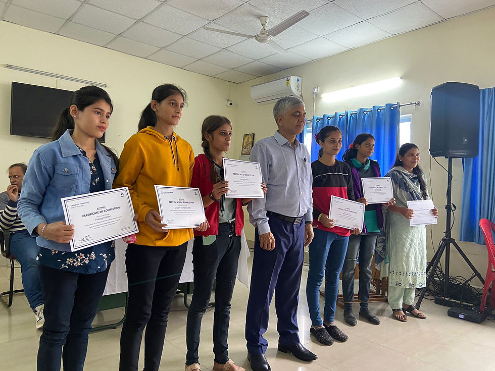 Six people hold certificates, smiling in a classroom with blue curtains. The mood is celebratory and the room is well-lit.