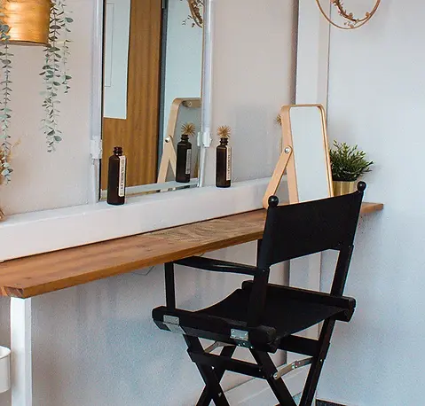 Im Studio von Laura steht ein schwarzer Schminkstuhl vor einem Spiegel.