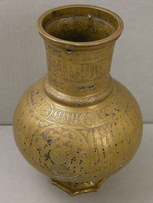 Late 13th-14th Century. Attributed to Egypt or Syria. Brass; engraved and inlaid with silver. Arabic inscription on on body: Glory to our Lord the Sultan / the kingly the Victorious Nasir al-Dunia wa al-Din Muhammad. Inscription on neck: His high Excellency, the Mamluk, the King, the Victorious. Inscription on body: His high Exellency, the Mamluk, the Wise, the Warrior, His Excellency, the Generous, the High, the Mamluk, the King, the Prince, the Leonine, the King, the Victorious. H. 10 1/4 in. (26 cm) Max. Diam. 7 1/4 in. (18.4 cm). Accession no.: 91.1.555.