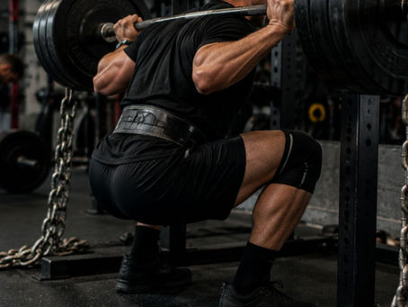Un levantador ejecuta una sentadilla pesada con cadenas y resistencia variable en una jaula de powerlifting. La escena muestra el esfuerzo controlado, la estabilidad del movimiento y la aplicación de sobrecarga progresiva en un entorno de gimnasio oscuro y realista, reflejando el uso estratégico de la resistencia para mejorar fuerza y potencia.