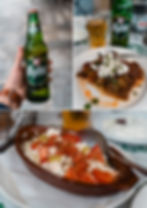 A hand holds a Mythos beer bottle. Nearby, plated Greek dishes with feta, tomatoes, herbs. Casual dining setting, relaxed mood.