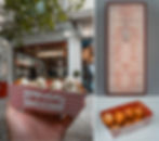Hand holding a red-striped box of Greek desserts with white drizzle in front of a shop. Menu and plain dessert box also shown.