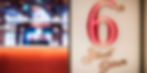 A red and gold sign that says '6th Street Diner'. Blurry in the background are 2 members of crew standing at the check in area.