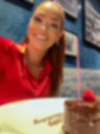 Chocolate cake with a candle on top with a happy birthday message on the plate and birthday girl posing behind it