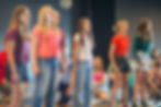 Several people standing and singing with others watching them in the background.