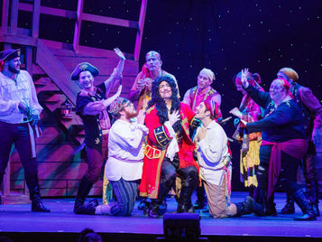 Performers in the "Peter Pan" musical on stage surrounding the actor portraying Captain Hook.