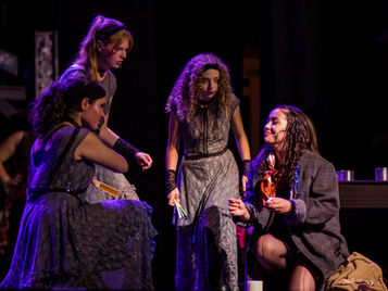 Four actors in conversation under stage lighting in a live theatrical scene.