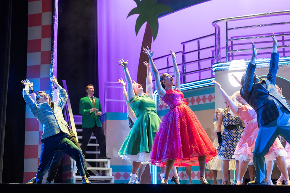 Actors on stage during a dance number with their hands raised up in the air.
