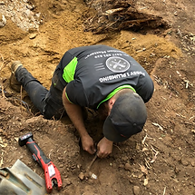 A plumber kneeling down in the dirt to locate pipes in teh ground to connect a new septic 