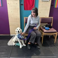 A lady sat next to her Golden Retriever dog holding a rosette after passing a training level at Guns and Noses