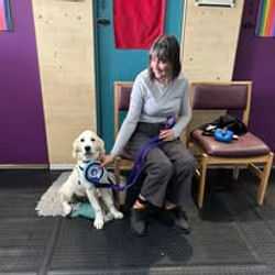 A lady sat next to her Golden Retriever dog holding a rosette after passing a training level at Guns and Noses
