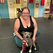 A lady sat next to her staffordshire bull terrier dog holding a rosette after passing a training level at Guns and Noses