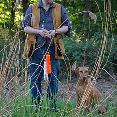 A gentleman stood next to a fox red labrador by a pond holding a gundog dummy in east yorkshire