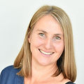 Monika hat schulter-lange blonde Haare. Sie trägt ein blaues Oberteil. Sie lächelt.