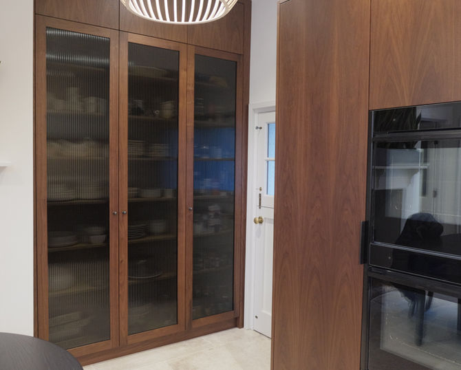 Floor-to-ceiling walnut larder cabinetry featuring smoked fluted glass doors, integrated appliances and bespoke storage