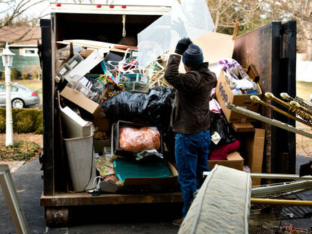 Worker loading junk and clutter into a dumpster truck.