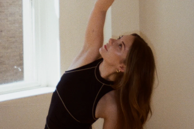 Woman stretching her arm up towards the window in a pilates pose