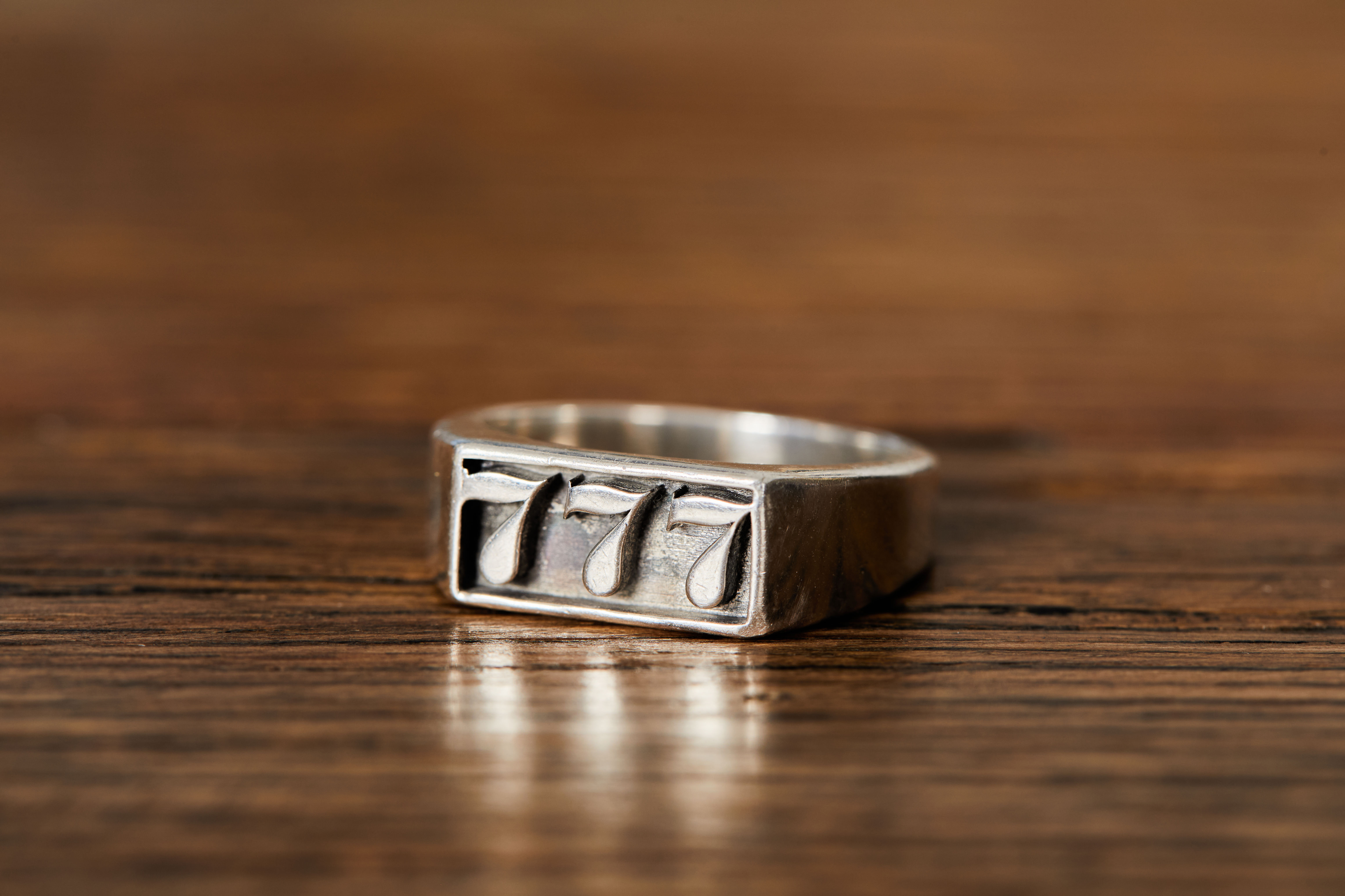 Sterling silver ring with raised 777 slot machine design on wooden background.